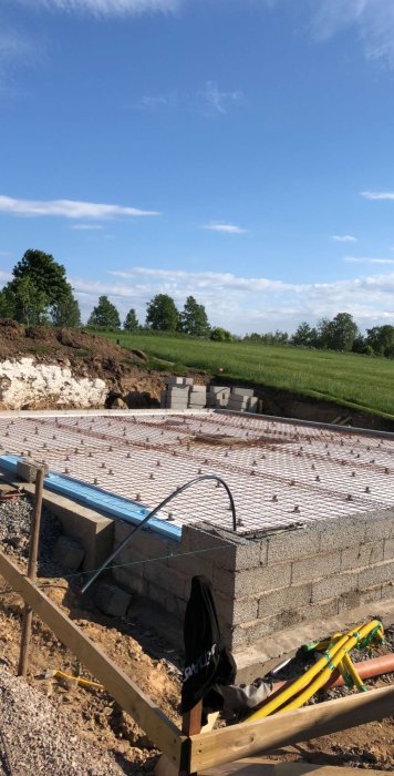 Grundläggning för hus med armeringsjärn och gjutformar klara mot blå himmel.