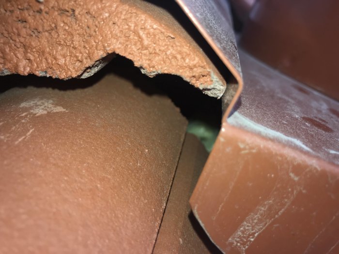 Närbild på takpannor där en panna har lyfts för att visa understrukturen och eventuell avsaknad av spikning.