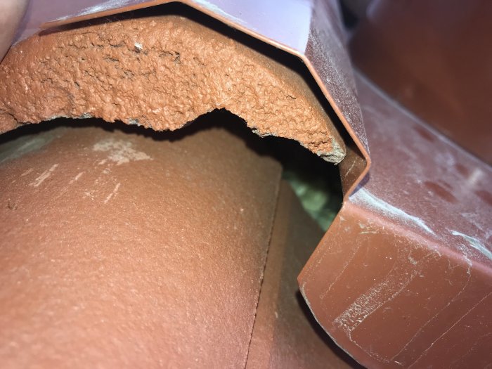 Närbild på takpannor där en panna är upplyft några centimeter för att visa underliggande struktur.