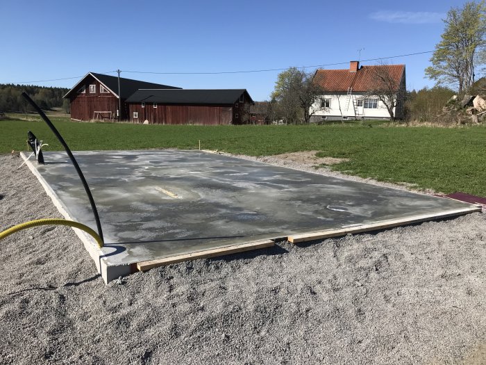 Nyutgjuten betongplatta med släta ytor på en byggarbetsplats framför landsbygdshus.