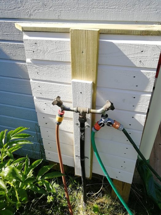 Uppvärmd vattenkran installerad på en vit trävägg med anslutna slangar i garaget.