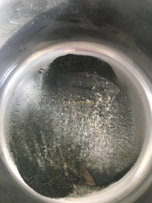 En smutsig vattenfilter på 10 micron efter tvätt, med synliga sediment och partiklar i botten av en metallbehållare.