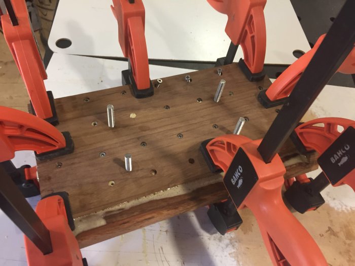 Trästeg klämt med orange tvingar under sammanfogning, förborrade hål och metallbultar syns.