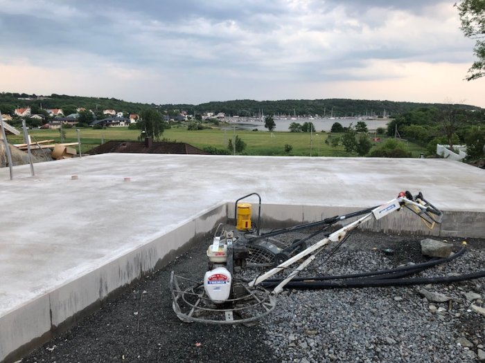 Nyutgjutna betongplattor med slipningsutrustning vid byggplats, med utsikt över vatten och grönområden.