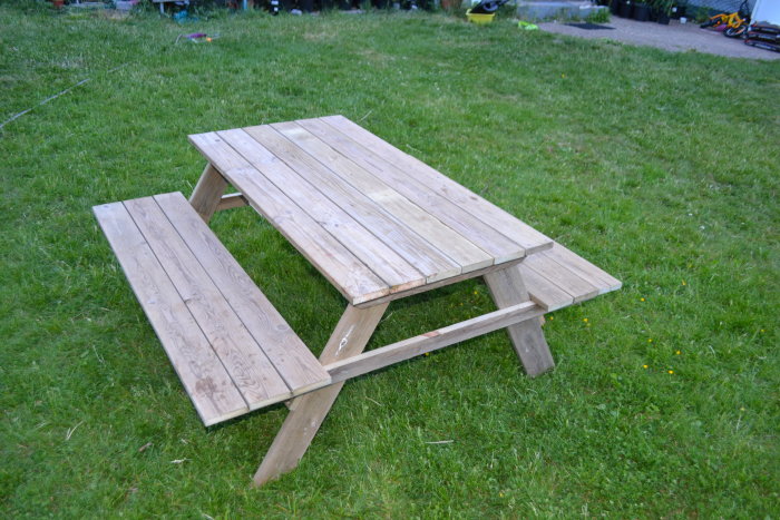 Ett hemmagjort picknickbord av återanvänt altangolv med platser för barn i en trädgård.