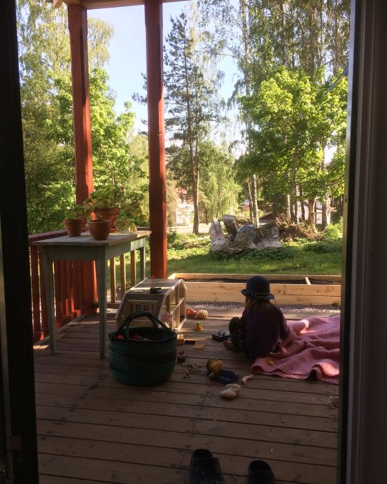 Utsikt från en veranda under konstruktion med trädgårdsutsikt, leksaker och en korg på trägolvet.