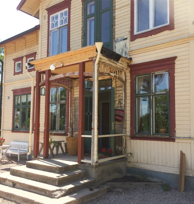 Renovering av en furstukvist på ett gult trähus med röda fönsteromfattningar och en ny snickrad veranda.