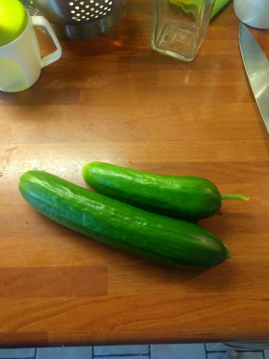 Två gröna slanggurkor ligger på ett träbord.