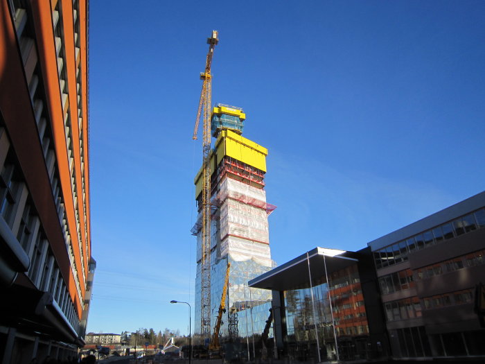 Byggarbetsplats med hisschakter för Victoria Tower i Kista, kran och byggningsställning mot blå himmel.