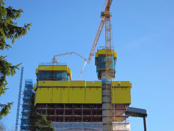 Byggarbetsplats med kranar och hisschakt på Victoria Tower i Kista under konstruktion mot en klarblå himmel.