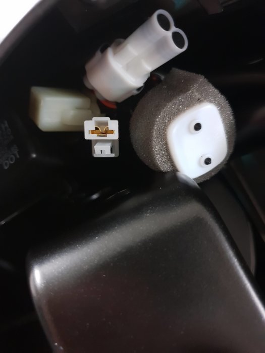 Elanslutningar under motorcykelsäte inklusive vit kontakt och flerpolig kontakt.