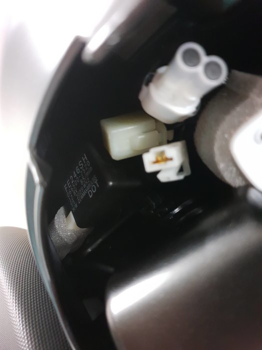 Elektriska anslutningar under sätet på en motorcykel med fokus på en vit kontakt.