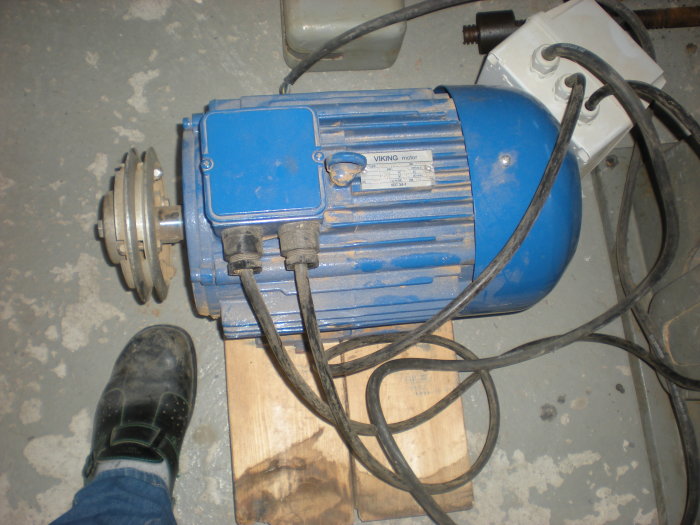 En blå industriell motor märkt "VIKING" på en betonggolv med elkablar och en person i arbetskläder ståendes framför.