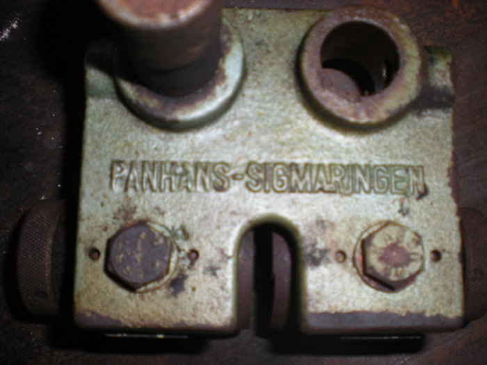 Rostig metallkomponent märkt 'PANHANS-SIGMARINGEN' med fästöron och en låsmutter.