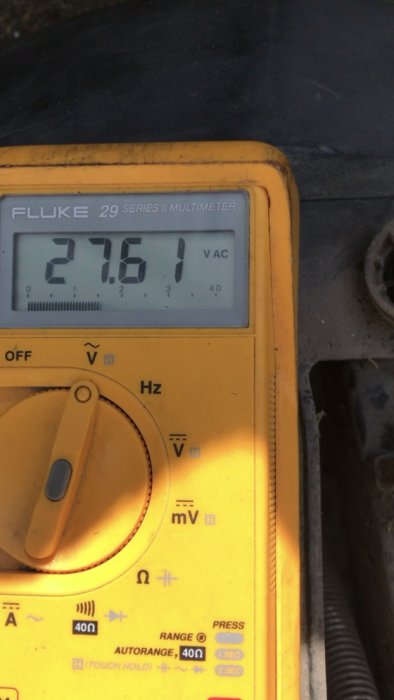 Multimeter visar en växelspänning på 27.61 V, indikerar en pulserande spänning i felsökningsprocess.