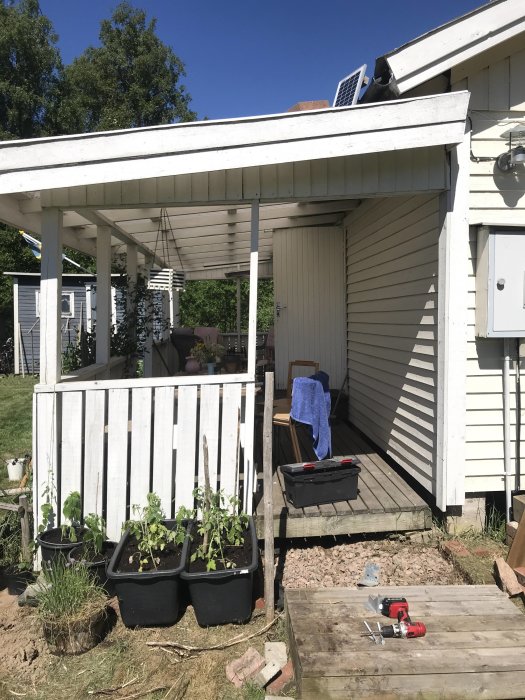 Altan med tak som har glidit från huset, verktyg på marken, planteringskärl framför.