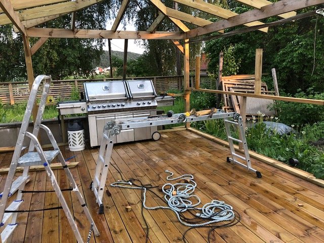 Pågående bygge av ett enkelt uterum med takstomme, grill och trall, samt verktyg och byggmaterial utspridda.