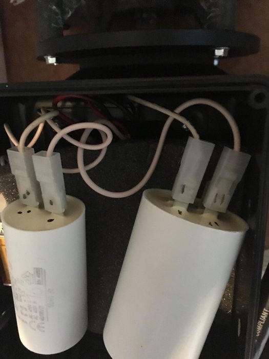 Två kondensatorer monterade i ett spabad, den ena ska bytas, båda med elektriska kablar anslutna.