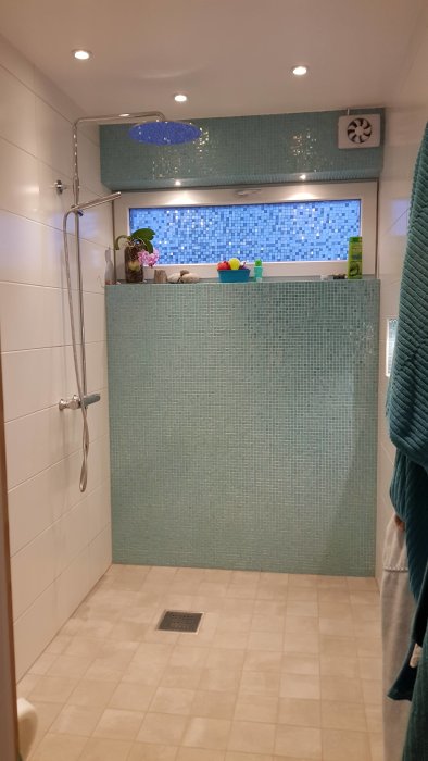 Renoverat badrum med glasvägg, mosaikplattor, och en blå duschkabin.