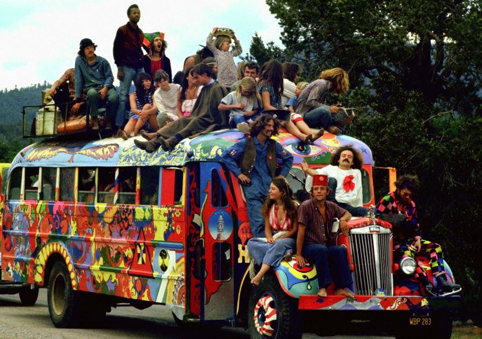 Människor i retrokläder på en färgglad hippiebuss, symbol för 60-talets frihetskultur.