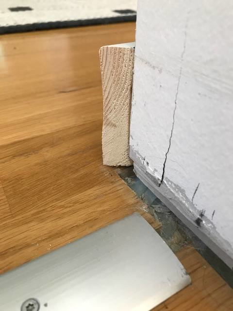 Golvsockel gersågad i 45 grader med en lätt konkav form, mot en vit vägg och ett trägolv.