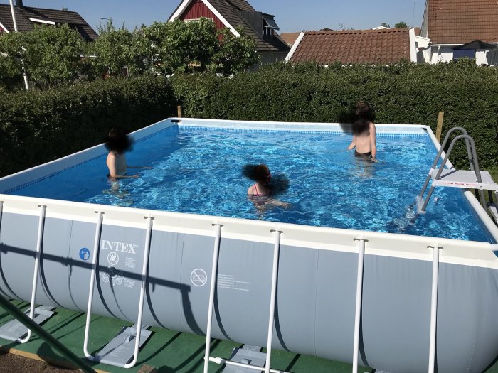 Familj badar i en uppsatt, rektangulär Intex-above-ground-pool med stege under solig dag.