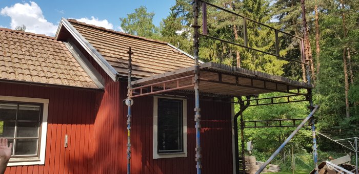 Renovering pågår med borttagna takpannor och byggnadsställningar vid röd trähusfasad.