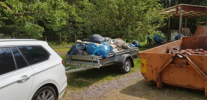 Släpvagn fullastad med säckar och skräp, redo för tippen, parkerad bredvid en container.