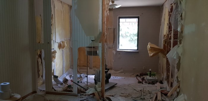 Kaotisk inomhus rivningsplats med synlig isolering, avrivna väggplattor och rivningsavfall på golvet.