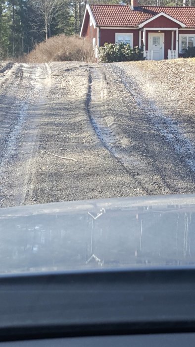 Uppkört och skadat område med spår efter tunga fordon framför rött hus, med fokus på förstört underlag.