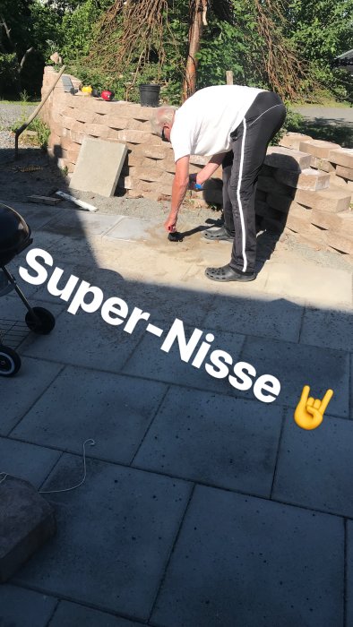 Man som lägger plattor utomhus med texten "Super-Nisse" och emojisymbol.