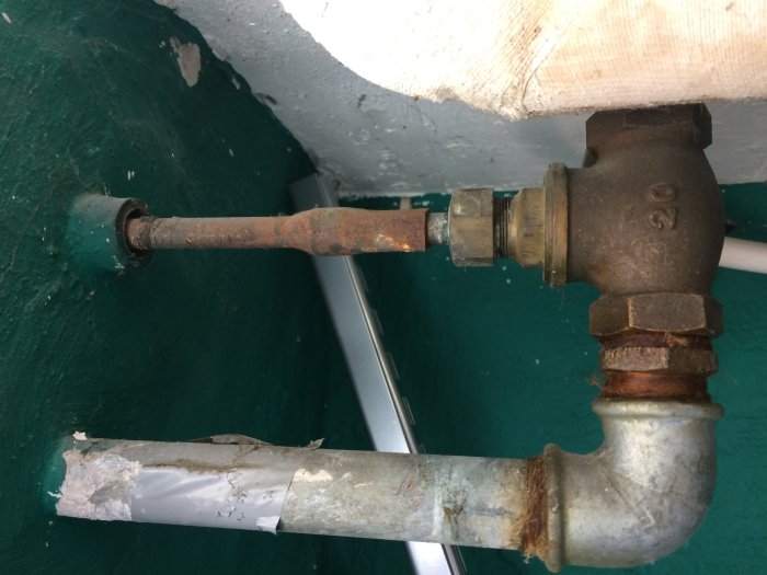 Gammal korroderad vattenutkastare med synliga packningar och tejp lindad runt ett rör, inomhusvy.