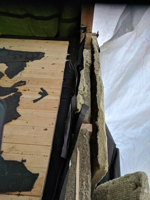 Byggkonstruktion med synliga reglar och isolering, delvis urholkade, vid en balkongrenovering.
