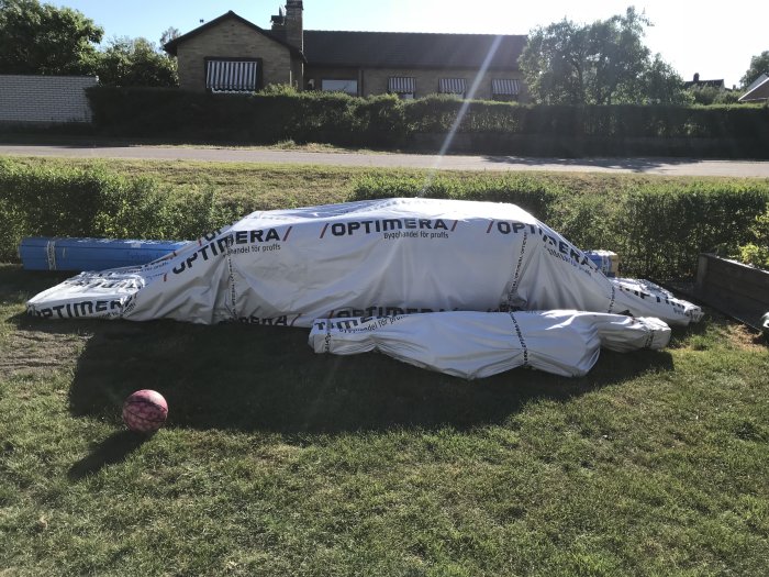 Inplastad virkesleverans från Optimera på en gräsmatta med en rosa boll i förgrunden.