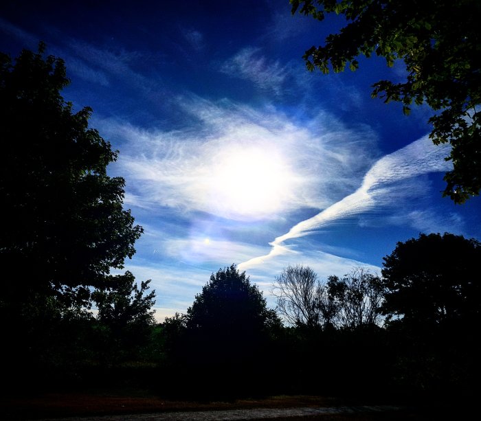 Morgonhimmel med solen som skiner och några träd i silhuett mot en dramatisk molnformation.