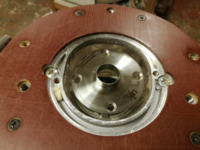 Fräshylsa monterad på träbord, synliga mäskruvar och urskuren öppning.