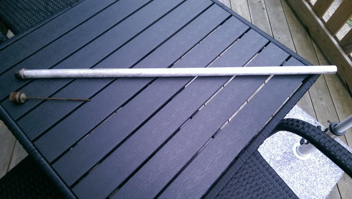 En lång metallstång och en rostig anod bredvid på ett mörkt trädäck.