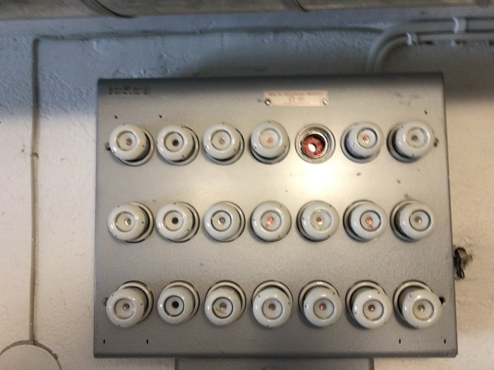Ett gammalt proppskåp med säkringar, en av dem bränd och rödmarkerad, i en suddig bild som ger en känsla av elproblem.