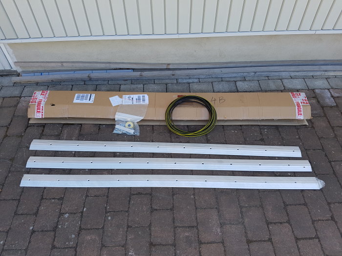 Oanvänd 6m lång Commercial Door tröskel med delar spridda på stenläggning.