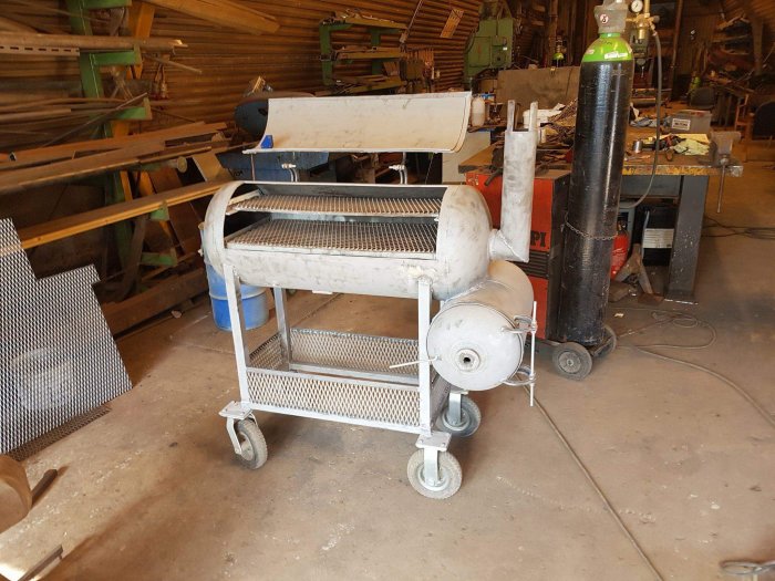 En gammal vit rullvagn med en perforerad metallhylla i ett rörigt verkstadsutrymme.