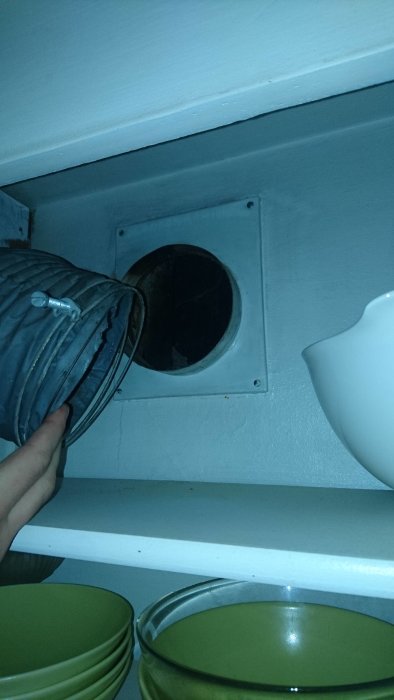 Hand håller bort ett ventilationsrör som visar en ventils öppning i köksskåp, utan synlig fläkt eller imkanal.