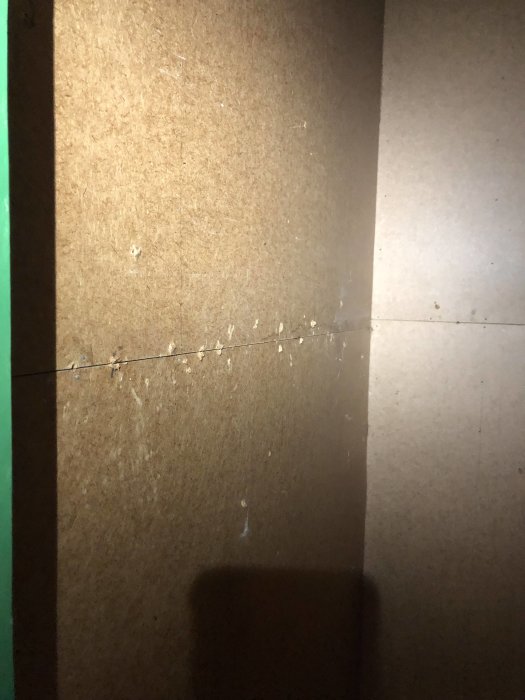 Obehandlad masonitvägg med synliga skarvar och små spikhål som behöver förberedas innan målning eller tapetsering.