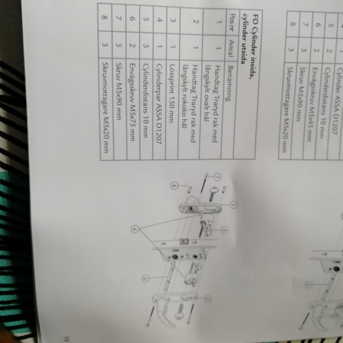 Suddig bild av en öppen installationsmanual för ett lås, med text och diagram över låskomponenter och deras montering.