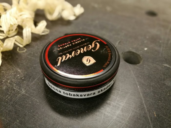 En dosa snus på ett snickarbord med träspån i bakgrunden.