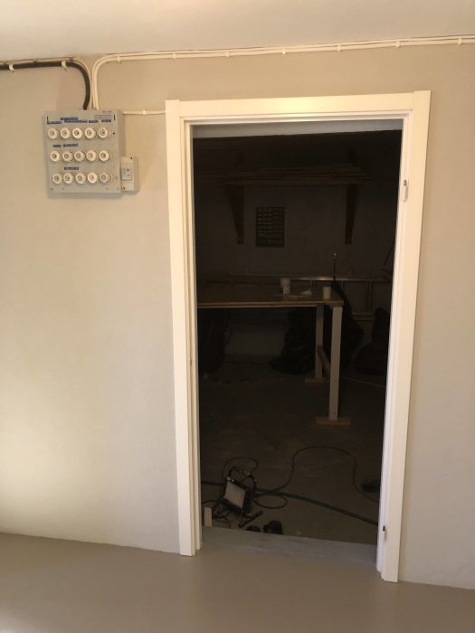 Renoverat rum med högblankt golv och vita väggar, dörröppning utan dörr, installationscentral till vänster.