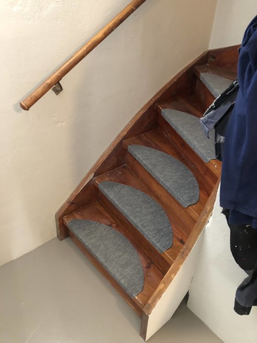 En trätrappa med gråa mattor på stegen, omgiven av nyrenoverade väggar och en träledstång.