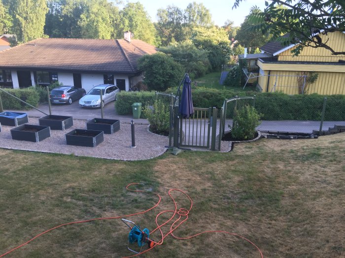 Trädgård med ny lagd kantsten runt gräsmattan, odlingslådor och utspridd grusgång.
