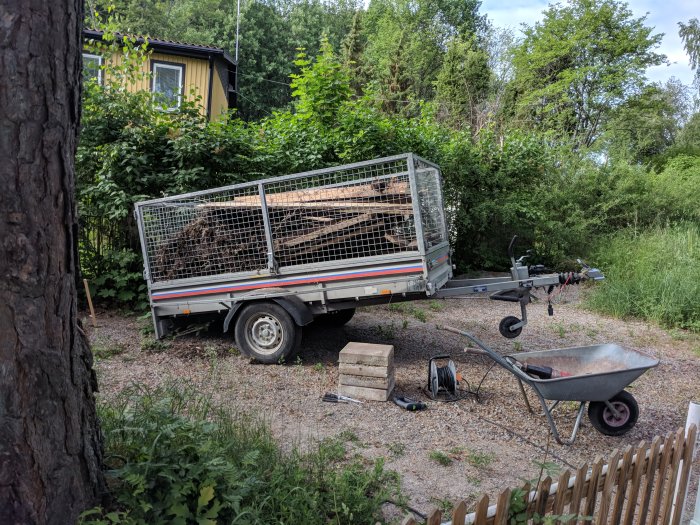 En överlastad släpvagn full av bråte parkerad bredvid en skottkärra och trädgårdsutrustning.