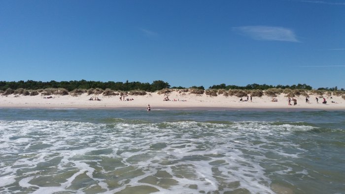 Strandvy med frigolitvågor och människor som solar och badar vid kusten.
