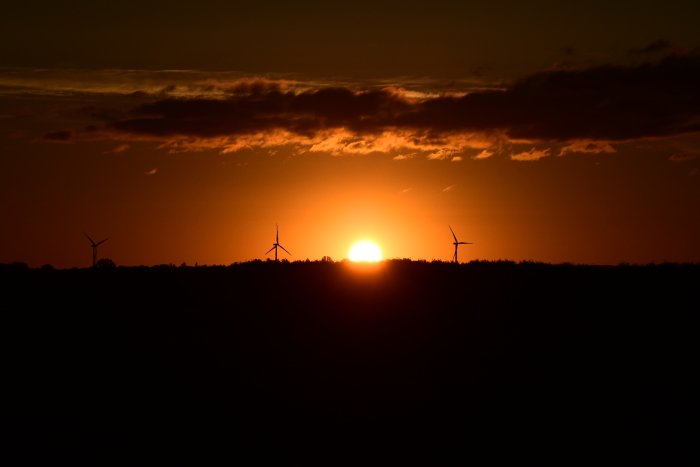 Solnedgång med vindkraftverkens silhuetter mot en dramatisk himmel.